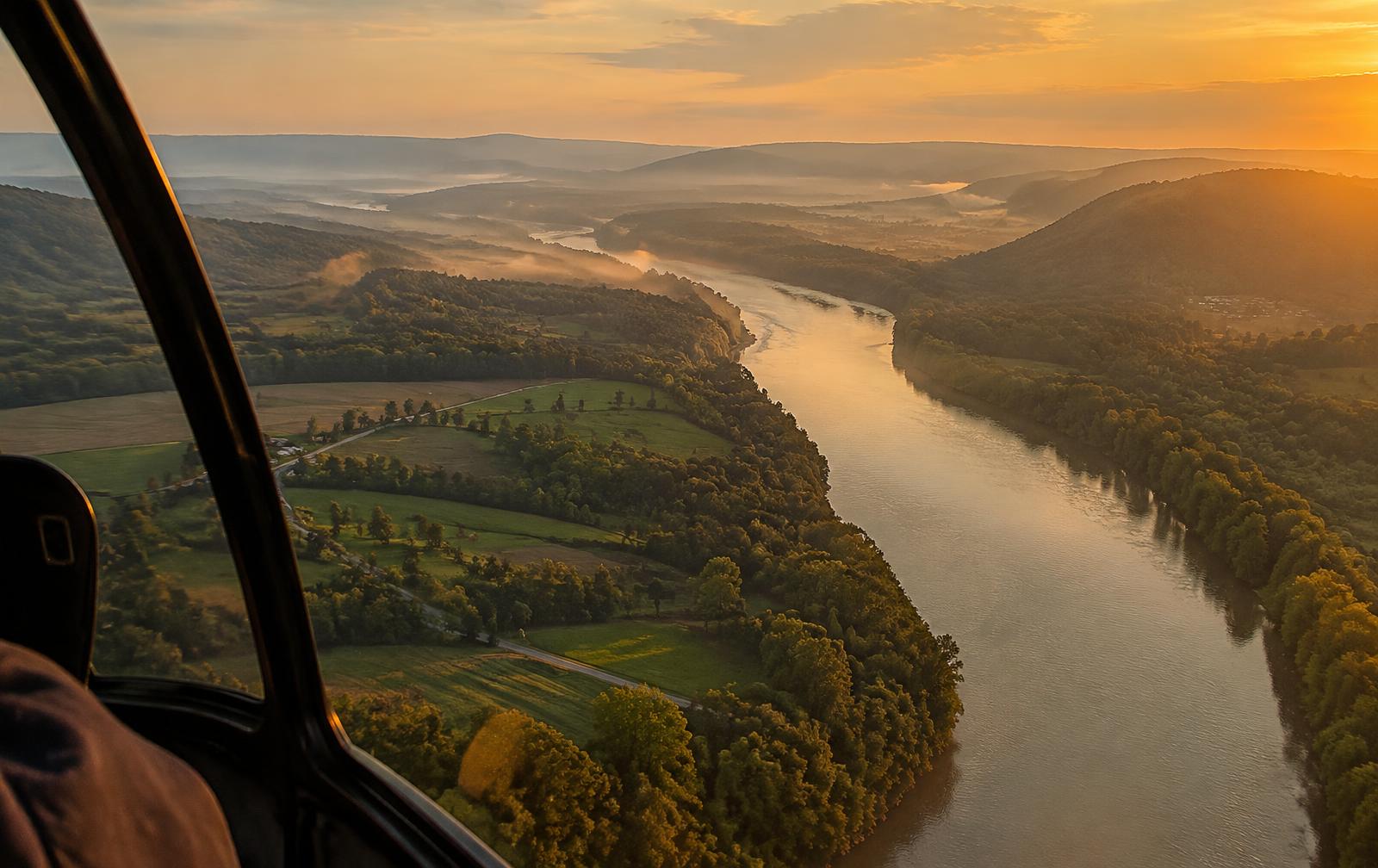 View from a helicopter window over a river valley at golden hour
